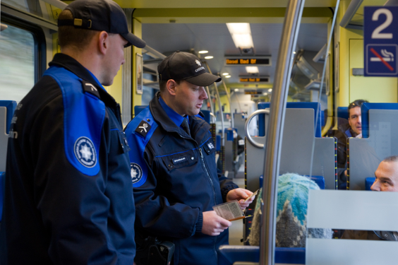 Due guardie di frontiera controllano la carta d'identità di un viaggiatori.